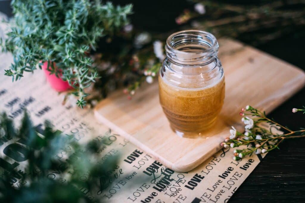 A bottle of honey on a wooden cutting board on a wooden table with green plants